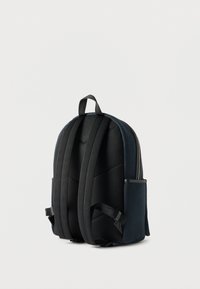 Συμπαγές σκούρο μπλε σακίδιο με επενδυμένους μαύρους ιμάντες ώμου, χειρολαβή στο πάνω μέρος και πλαϊνές τσέπες, παρουσιάζεται σε απλό φωτεινό φόντο.