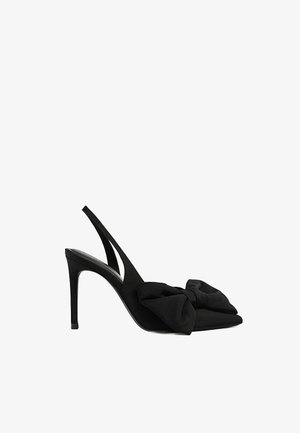 Czarny sandał na wysokim obcasie typu slingback z ostrym czubkiem i dużą ozdobną kokardą z materiału z przodu, na białym tle.