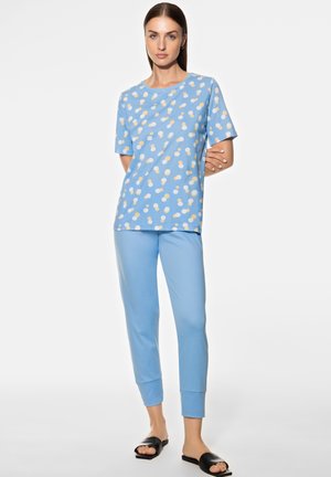 Himmelblaues Baumwoll-Pyjama-Set mit einem kurzärmeligen Oberteil mit gepunktetem Muster und passenden, umschlägigen Hosen, kombiniert mit schwarzen Schlüpfsandalen.