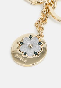 Gold-tone metal keychain featuring a circular pendant with a glittering silver flower design and green accents, labeled "Furla."