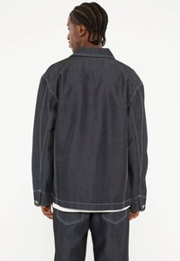 Donkerdenimjacket met een ruime pasvorm, voorzien van contrasterende stiksels, een puntige kraag en met knopen sluitende mouwen. Draag het over een wit kledingstuk.