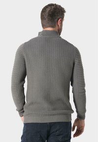 Grauer Strickpullover mit hohem Kragen, der strukturierte Rippmuster an den Schultern und Ärmeln sowie einen taillierten Saum aufweist.