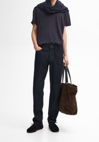 Mörkblå jeans, t-shirt med kort ärm i marinblått och en mörk scarf. Modellen håller en brun mockaväska och har på sig svarta loafers.