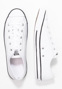 WeißeCanvas-Sneaker mit schwarzem Gummibezug, Schnürung auf der Vorderseite, strukturiertem Innenfutter und klassischem Low-Top-Design mit runder Zehenpartie.