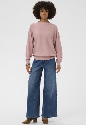 Svjetloružičasti pulover širokog izreza i rebrastog poruba, upareni s labavim plavim trapericama. Outfit upotpunjuju smeđe cipele s debelom petom.