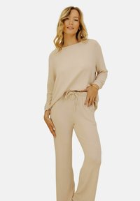 Ensemble de vêtements de détente beige avec un haut à manches longues ample et un pantalon à cordon, présentant une texture douce et une coupe décontractée.