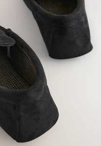 Sorte ruskinds-sutsko med rund tå og struktureret indvendig, med lav hæl og sømløst design.