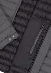 Grå vadderad jacka med en blandning av quiltade och släta tygtexturer, med en dragkedjeförsedd ficka och knappstängning.