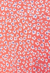 Tissu rouge à motif floral, présentant de petites fleurs blanches aux centres bleus, avec une texture lisse. Détail de couture visible en haut.