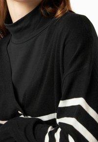 Maglione nero a maglia con collo alto e strisce orizzontali bianche sulle maniche. Texture morbida e design a vestibilità rilassata.