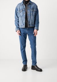 Ljusblå denimjacka med framfickor och knappstängning. Svart zip-halströja under, tillsammans med blå jeans och svarta stövlar.