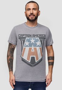 Šedé bavlněné tričko s grafickým designem štítu Kapitána Ameriky, modrá hvězda a hnědé akcenty, kulatý výstřih, krátké rukávy.