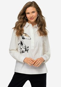 Camicia bianca a maniche lunghe con colletto, caratterizzata da ricami di animali neri e beige sul lato sinistro. Tessuto morbido e vestibilità rilassata.
