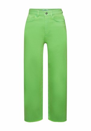 Femme portant un cardigan court lavande, un bralette blanc, un jean vert citron taille haute et court, ainsi que des sandales noires à enfiler, sur fond bleu.
