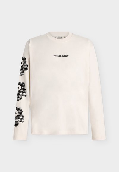 Млечнобяла риза с дълги ръкави с черен текст "marimekko" на гърдите и три големи черни цветни щампи на ляв ръкав.