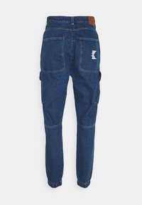 Pantalones cargo de denim azul con puños elásticos, dos bolsillos traseros y un parche con el logo cerca de la cintura. Presentan un corte relajado y un material duradero.