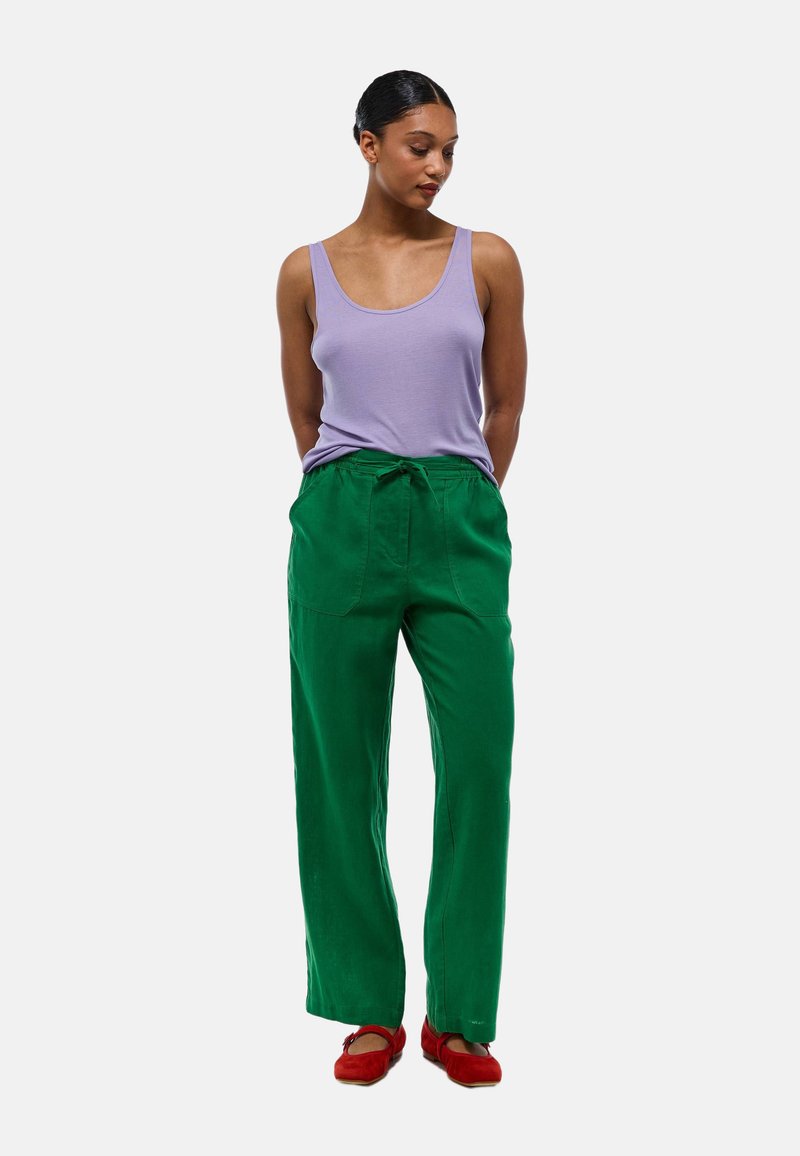 Débardeur violet, pantalon large vert avec cordon de serrage, et chaussures rouges. Détails notables : poches sur le pantalon. Texture lisse.