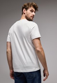 Valkoinen lyhythihainen t-paita, jossa on pyöreä kaula-aukko, yhdistettynä sinisiin farkkuihin. Kankaan pinta näyttää pehmeältä ja sileältä.