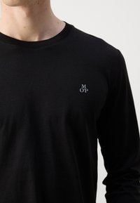 Sort langærmet t-shirt lavet af bomuld, med et lille hvidt logo "MOP" på venstre brystområde. Glat tekstur og tætsiddende design.