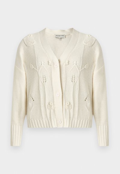 Μπεζ πλεκτή ζακέτα με λουλουδάτα σχέδια πλεξίματος, V-λαιμόκοψη, μακριά μανίκια, ριμπ μανσέτες και τελείωμα, και μπροστινό κούμπωμα με κουμπιά.