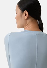 Chemise à manches longues bleu clair. Tissu lisse et ajusté avec un col rond et une couture dans le dos. Design minimaliste et sans couture.