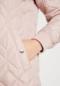 Lys pink quiltet jakke med diamantmønster og ribbede manchetter. Inkluderer en trykknapdetalje på lommen. Glat tekstur.