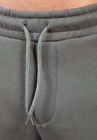 Gray sweatpants featuring a textured fabric, elastic waistband with braided drawstrings, and side pockets. Close-up view of details.