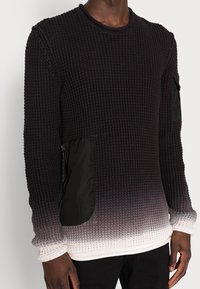 Pull-over en tricot noir texturé avec un effet ombragé dégradant vers le blanc. Comprend des poches latérales en tissu noir. Col rond, poignets côtelés.