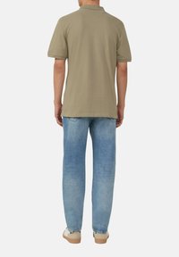 Olijfgroene polo met korte mouwen gecombineerd met lichtblauwe denim jeans. Het shirt heeft een kraag en een rechte zoom, gemaakt van een soepele katoenen stof.