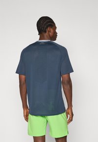Camisa atlética de manga corta en color navy con panel trasero texturizado y cuello redondo, combinada con pantalones cortos de color verde brillante.