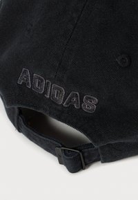 Nærbilde av svart justerbar baseballcaps med brodert "ADIDAS"-logo på stroppen bak mot hvit bakgrunn.