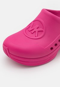 Sabot rose vif à enfiler avec semelle texturée et trous de ventilation, comportant le logo MK en relief sur le devant.