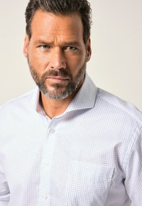Camisa blanca de botones con un pequeño patrón geométrico azul, presenta un cuello extendido y un bolsillo en el pecho, confeccionada en un tejido suave.
