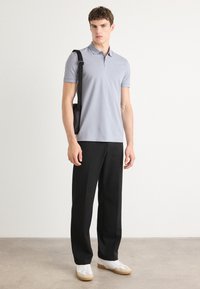 Polo de color azul claro en tejido suave, combinado con pantalones anchos negros y zapatillas blancas. Presenta mangas cortas y un ajuste relajado.