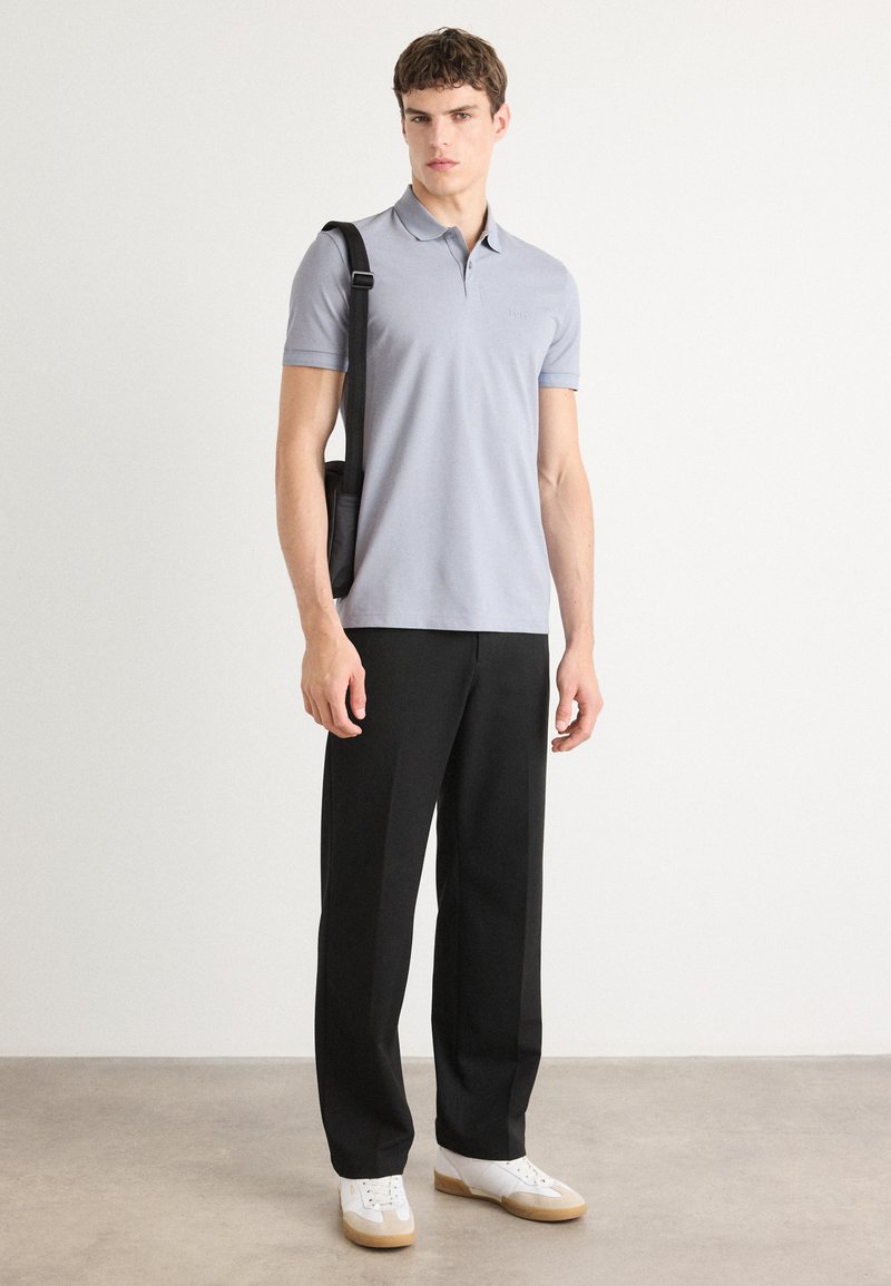 Hellblaues Poloshirt aus weichem Stoff, kombiniert mit schwarzen weiten Hosen und weißen Sneakers. Verfügt über kurze Ärmel und einen entspannten Schnitt.