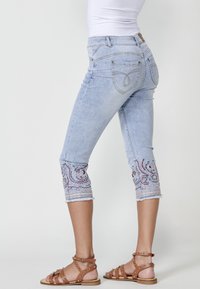 Light blue capri jeans with embroidered patterns at the hems, frayed edges, and a fitted design. Features two back pockets.