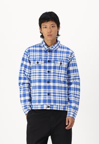 Blauw en wit geruite hemdenjasje met kraag, knoopsluiting aan de voorkant en twee borstzakken. Gemaakt van stof met een gestructureerd gevoel.