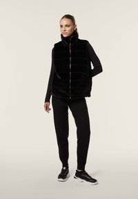 Mustat tekoturkiskaulustus, jossa on pystysuorat raidat, korkea kaulus ja vetoketjullinen etuosa. Päällä musta pitkähihaisen paita ja parina mustat housut sekä lenkkarit.