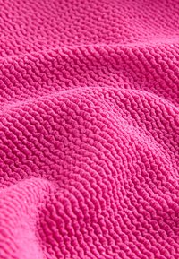 Tissu texturé rose avec un motif ondulé, présentant une surface douce et pelucheuse avec des paillettes subtiles. Convient pour des couvertures ou du rembourrage.