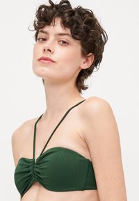 Zöld, bordázott bikini felső, bandeau kialakítással, vékony, állítható pántokkal és ráncolt középső részletettel. Sima textúra az egész felületen.