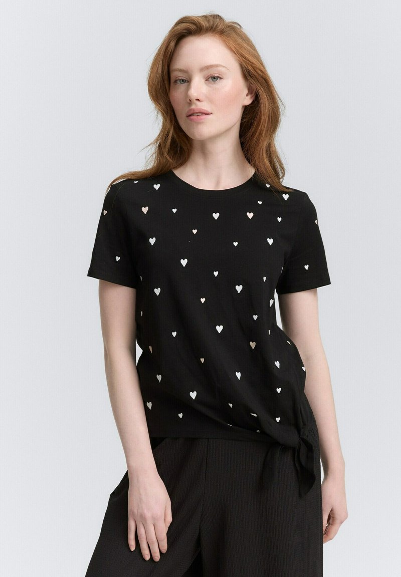 Czarna koszulka z okrągłym dekoltem, z wzorem małych białych i różowo-złotych serc. Związana w talii, wykonana z miękkiego materiału.