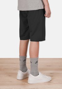 Svarta bomullsshorts med sidfickor, tillsammans med grå strumpor med en logotyp, och vita sneakers på ett trägolv.