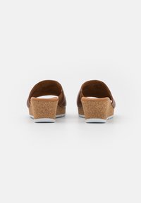 Sandales à talons compensés en cuir brun avec un talon en liège et une semelle en caoutchouc blanche, présentant un dos ouvert et une texture lisse. Design minimaliste.