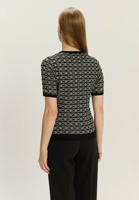 Sweter z krótkim rękawem w czarno-kremowym kolorze z geometrycznym wzorem. Wykonany z dzianiny, z ściągaczami przy mankietach i u dołu, w dopasowanej sylwetce.