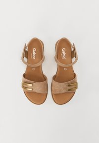 Tan suede sandals with a wide strap, featuring a metallic double buckle accent and an adjustable ankle strap. Flat sole.