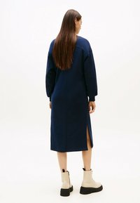 Navyblaue Midi-Robe mit langen Ärmeln, seitlichen Schlitzen und einem lockeren Schnitt; kombiniert mit beigen Ankle Boots mit einer robusten schwarzen Sohle.