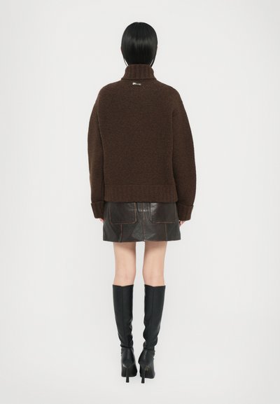 Brauner gestrickter Rollkragenpullover mit entspannter Passform, Wollstruktur und geripptem Saum, kombiniert mit einem schwarzen Leder-Minirock und kniehohen Stiefeln.