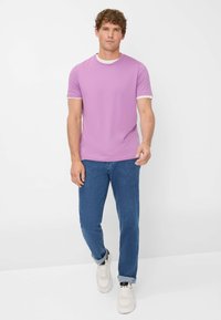 T-shirt viola a maniche corte con colletto a costine bianco, abbinato a jeans denim blu e sneakers bianche. Tessuto di consistenza liscia.