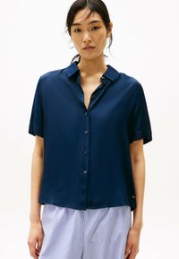 Camisa de manga corta azul marino con cierre de botones en la parte frontal y cuello clásico. Textura suave y corte relajado, combinada con pantalones a rayas.
