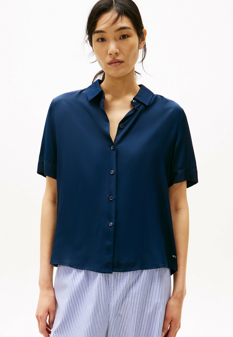 Camisa de manga corta azul marino con cierre de botones en la parte frontal y cuello clásico. Textura suave y corte relajado, combinada con pantalones a rayas.